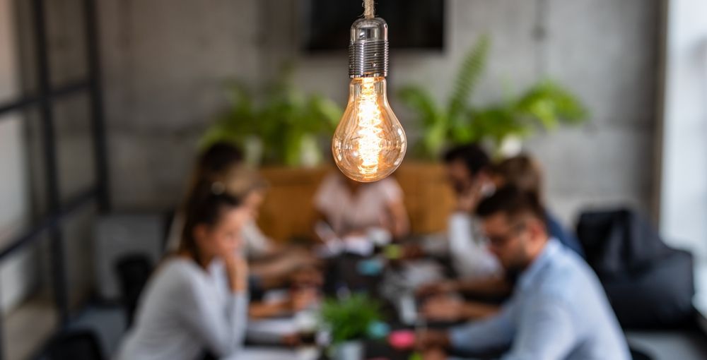 Glowing lightbulb hanging over a blurred office meeting.