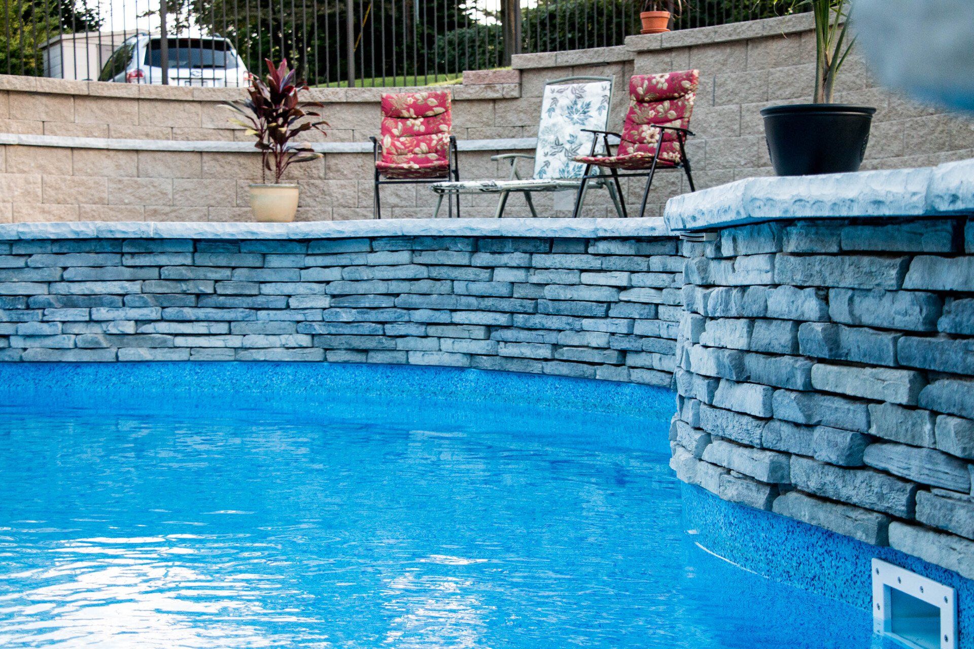 A swimming pool with a stone wall and chairs in the background.