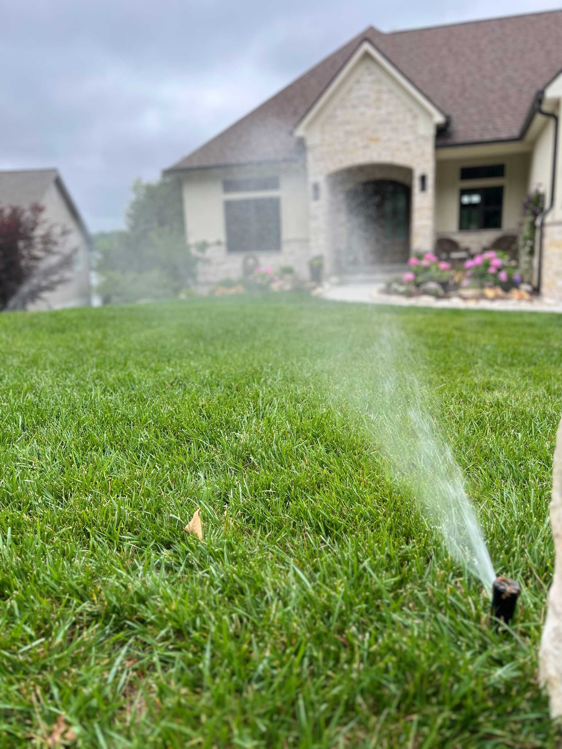 A sprinkler is spraying water on a lush green lawn in front of a house.