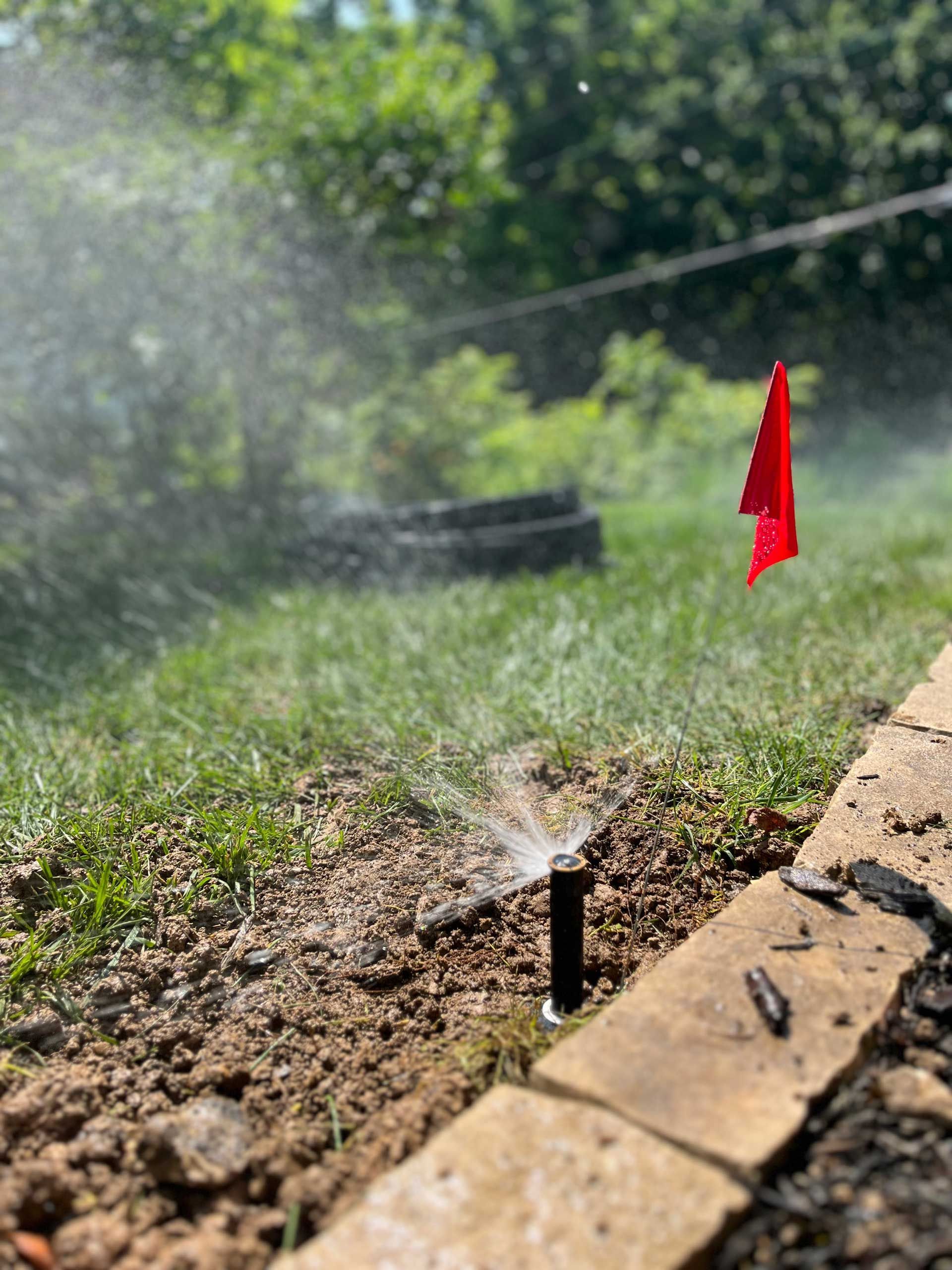 A sprinkler is spraying water on a lawn next to a red flag.