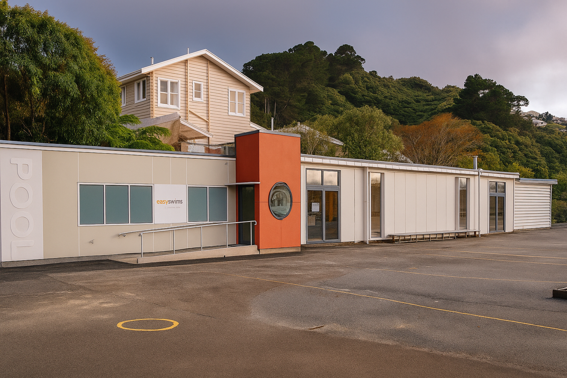 School building with a beige and orange facade, trees in the background, and a cloudy sky.
