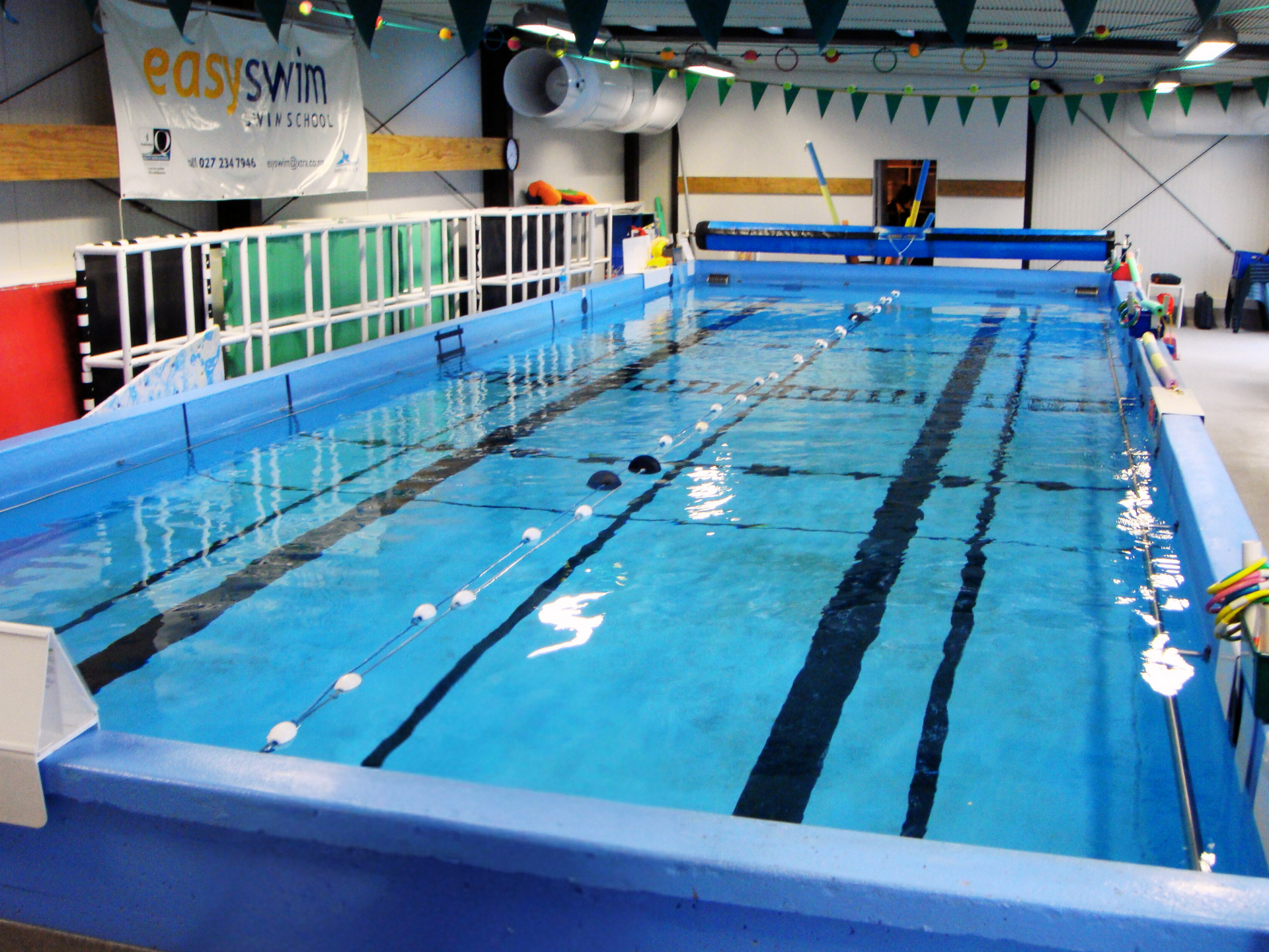 Indoor swimming pool, blue water, lane markers, white floats, empty, with 'easySwim' sign.