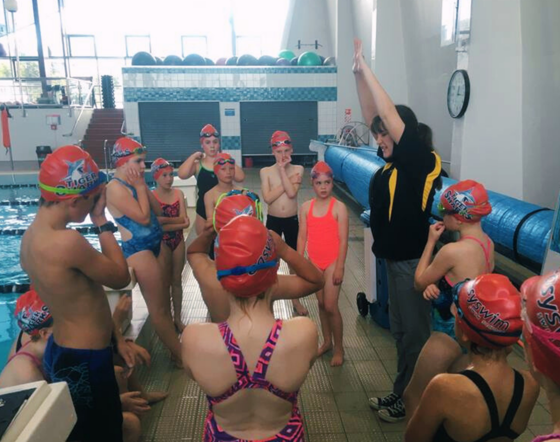 A swim coach instructing a group of children at a pool.