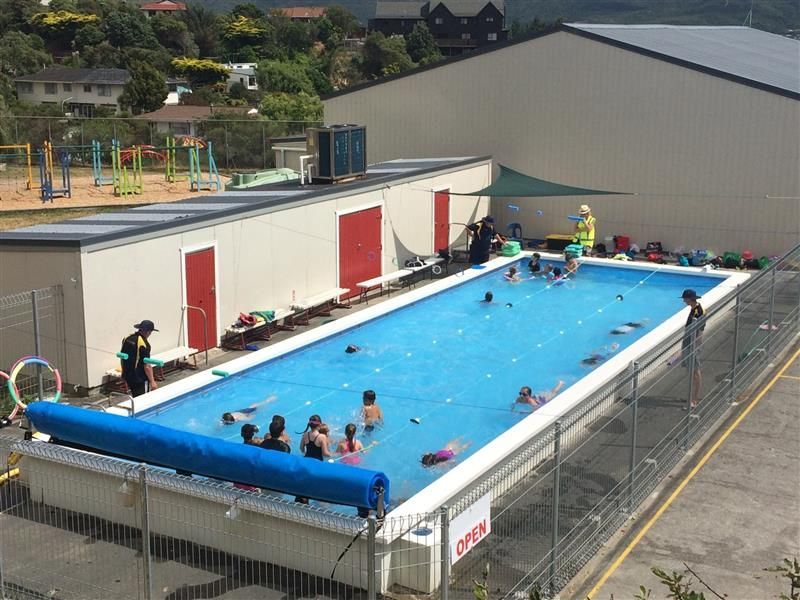 Outdoor swimming pool with children swimming, supervised by adults. Blue water, sunny day.