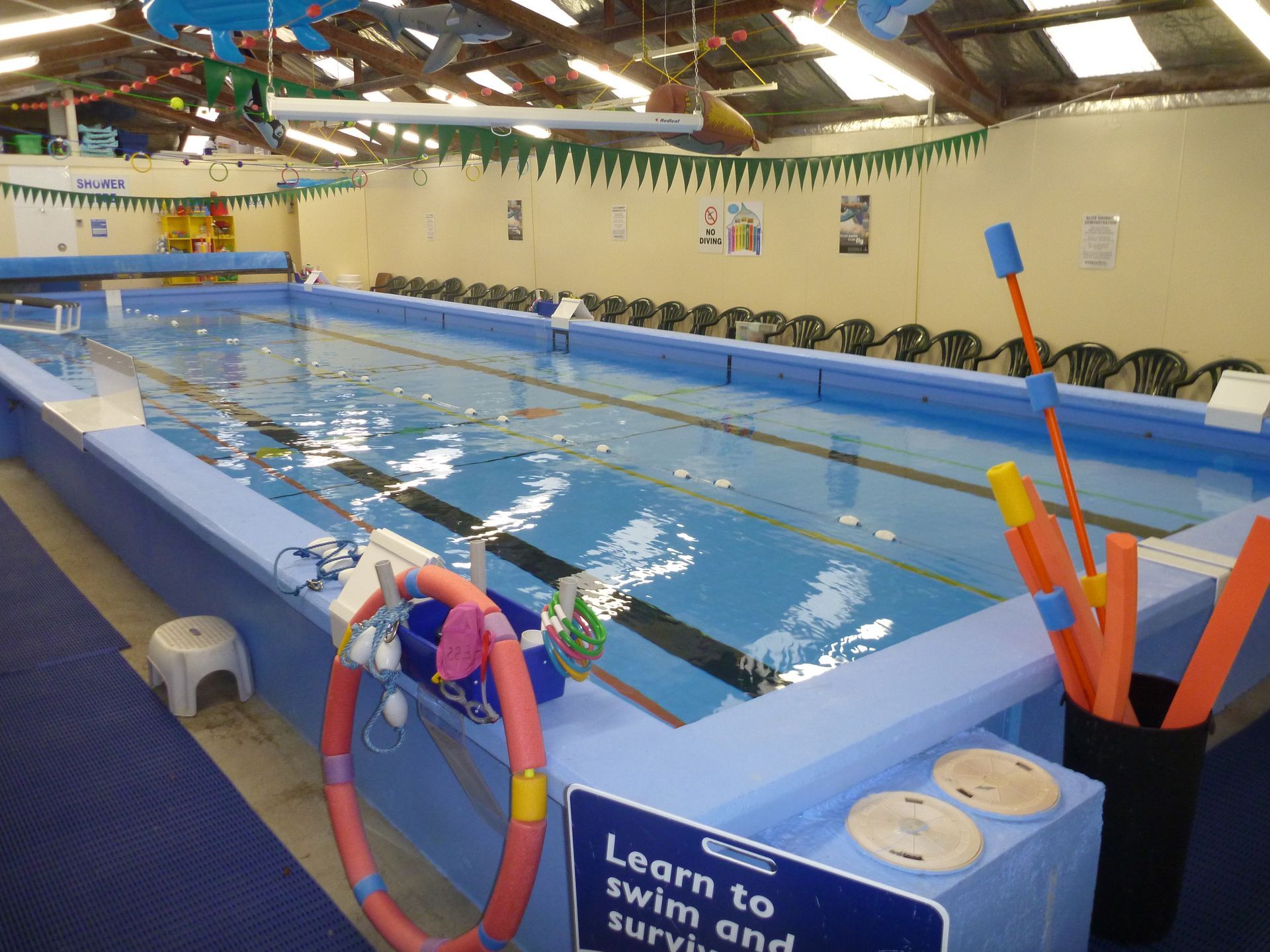 Indoor swimming pool with blue water, lane lines, and colorful flotation devices.