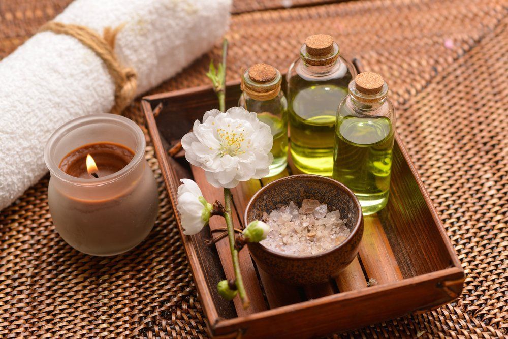 A Wooden Tray Filled With Bottles Of Essential Oils, A Candle, And Flowers — Bathurst JP Thai Massage In Bathurst, NSW
