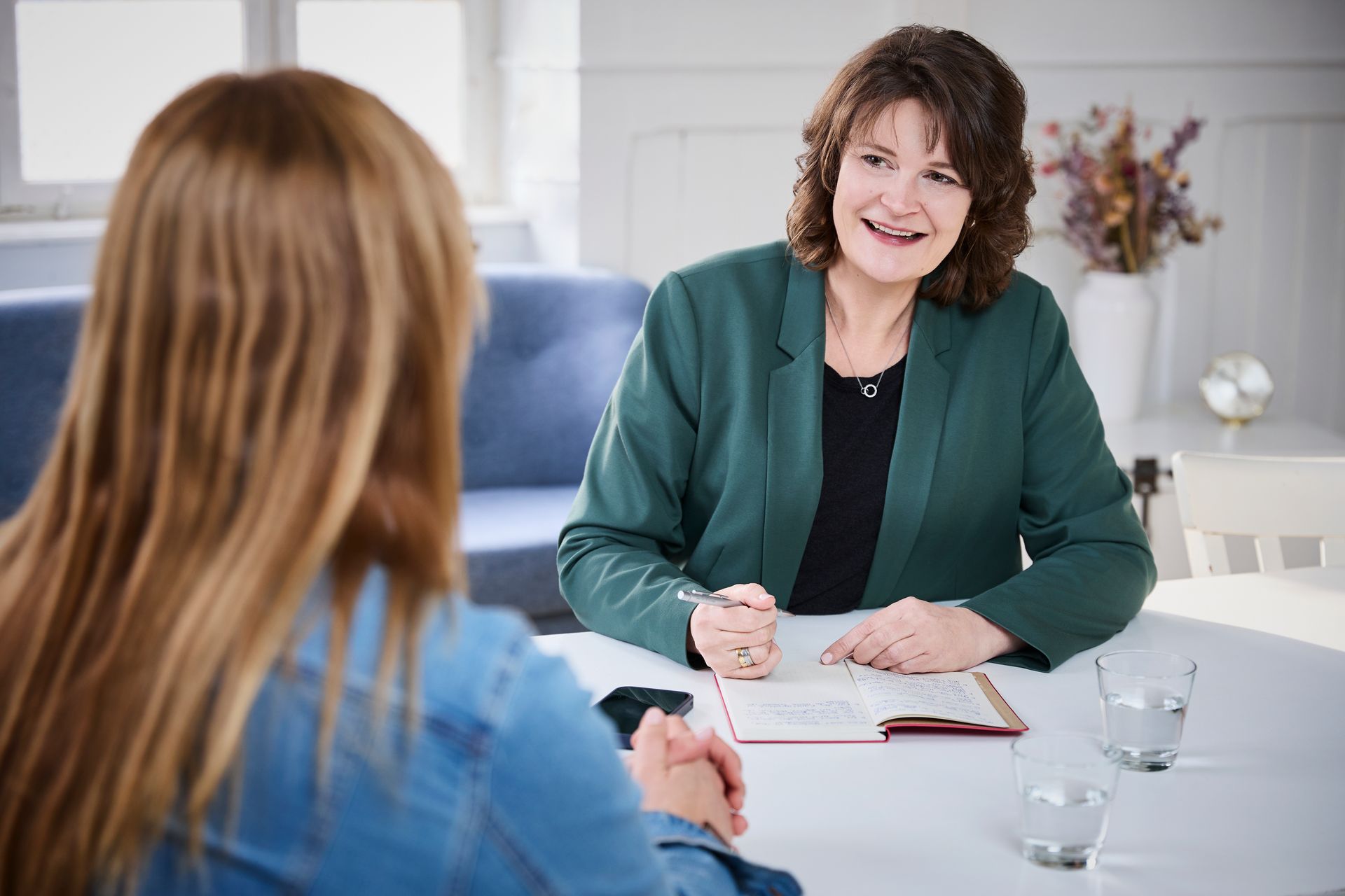 Eine Frau sitzt auf einem Stuhl und hält einen Stift und ein Notizbuch in der Hand.