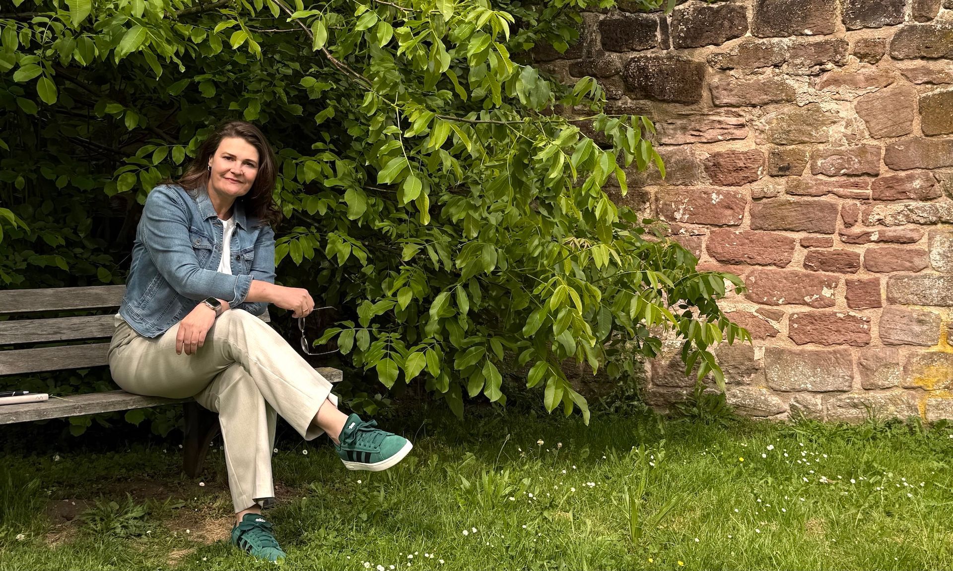 Eine Frau sitzt auf einer Holzbank vor einer Backsteinmauer.