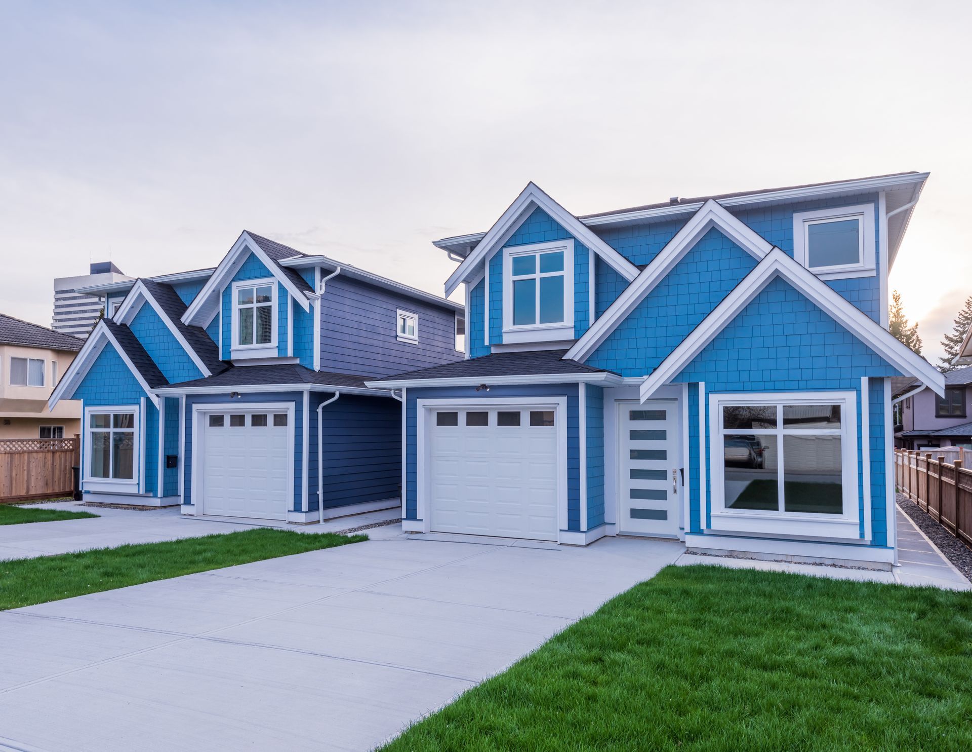 Two blue houses with white garage doors and green lawns, gray driveways, clear sky.