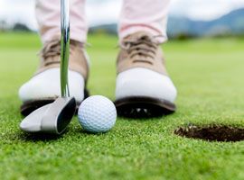 A person is putting a golf ball into a hole on a golf course.