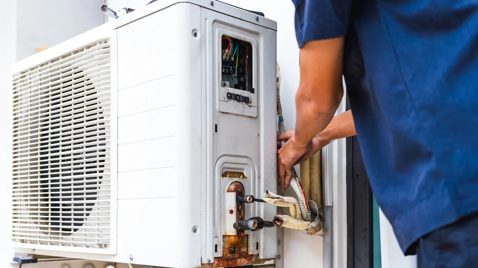 Person repairing a white outdoor air conditioning unit attached to a wall.