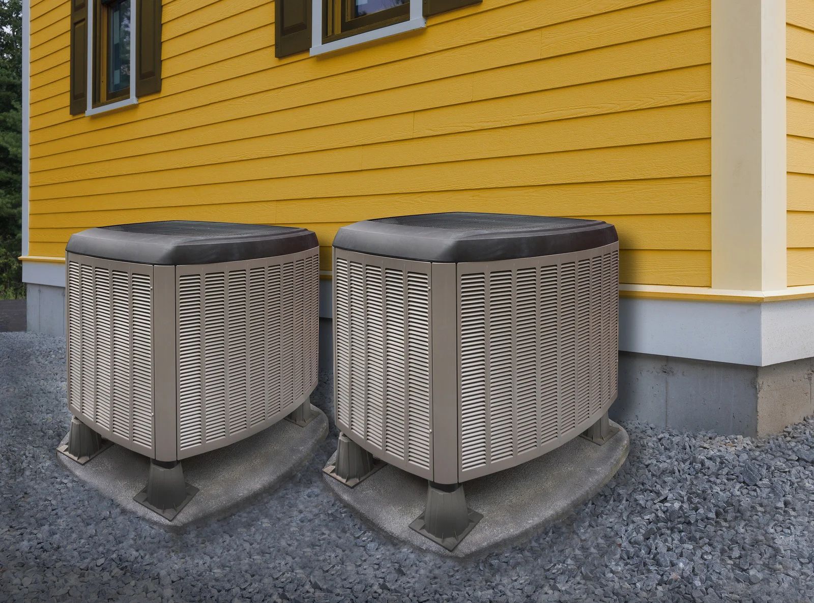 Two outdoor air conditioning units installed on concrete pads beside a yellow house.