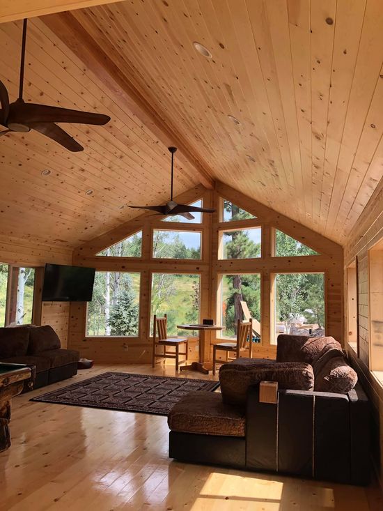 A living room in a log cabin with a vaulted ceiling and lots of windows.