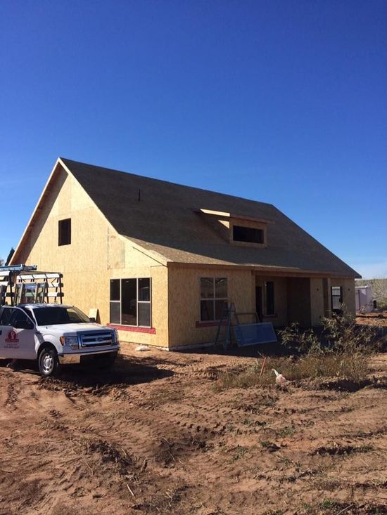 A white truck is parked in front of a house under construction.