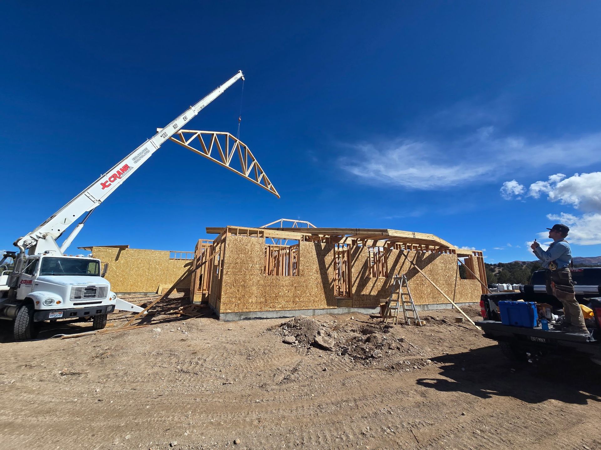 A crane is lifting a truss over a building under construction.