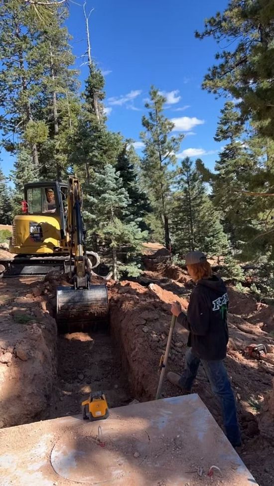 A man is standing in front of a bulldozer digging a hole in the ground.