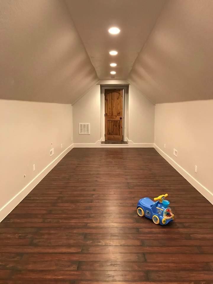 A blue toy car is sitting on a wooden floor in an empty room.