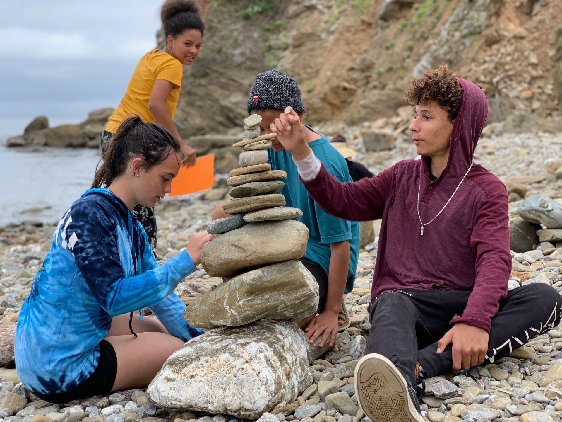 Montessori children are sitting on the beach stacking rocks