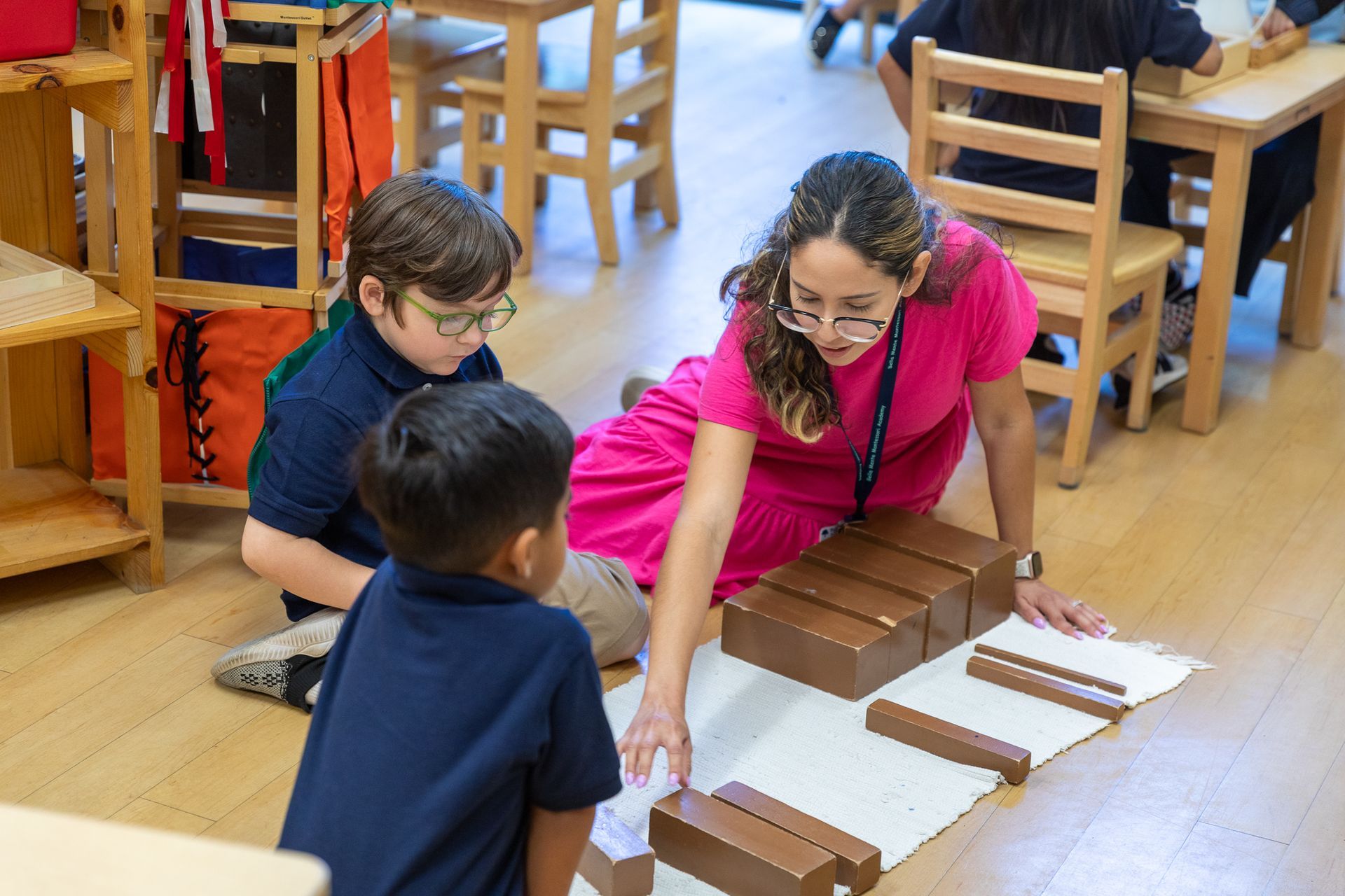 A Montessori guide in a pink shirt is working with children in a classroom.