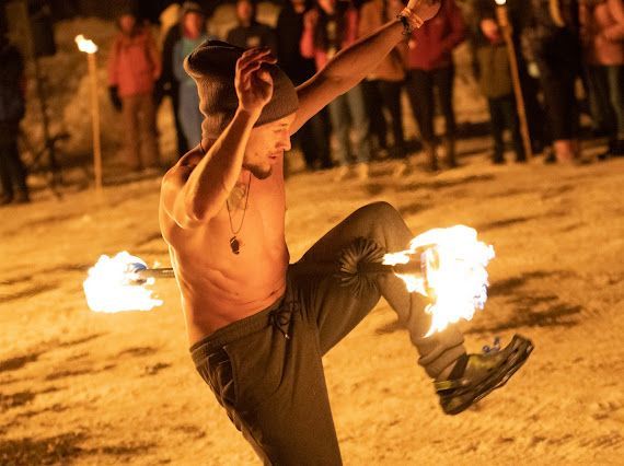 A shirtless man is dancing with fire in front of a crowd.