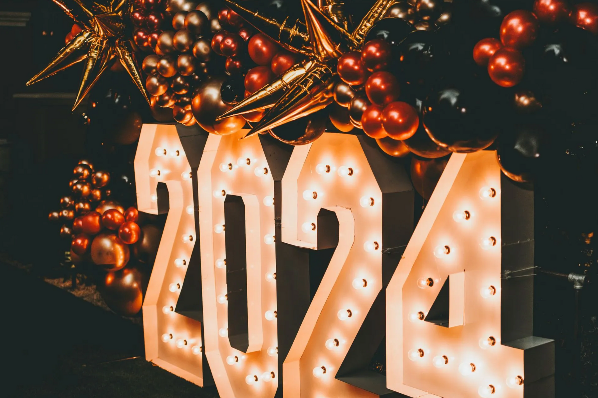 A sign that says 2024 is surrounded by balloons and lights.