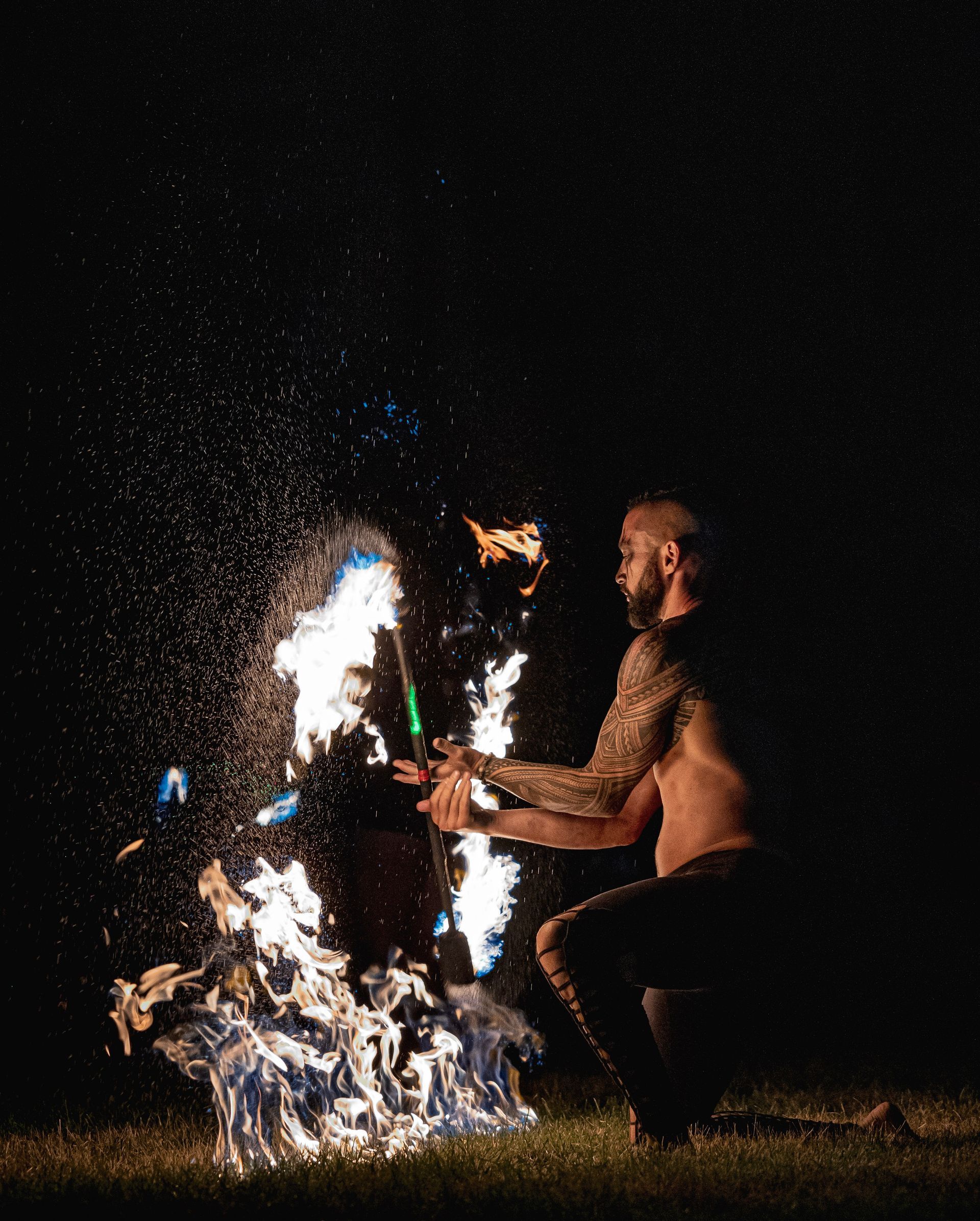 A man is kneeling down in front of a fire at night.