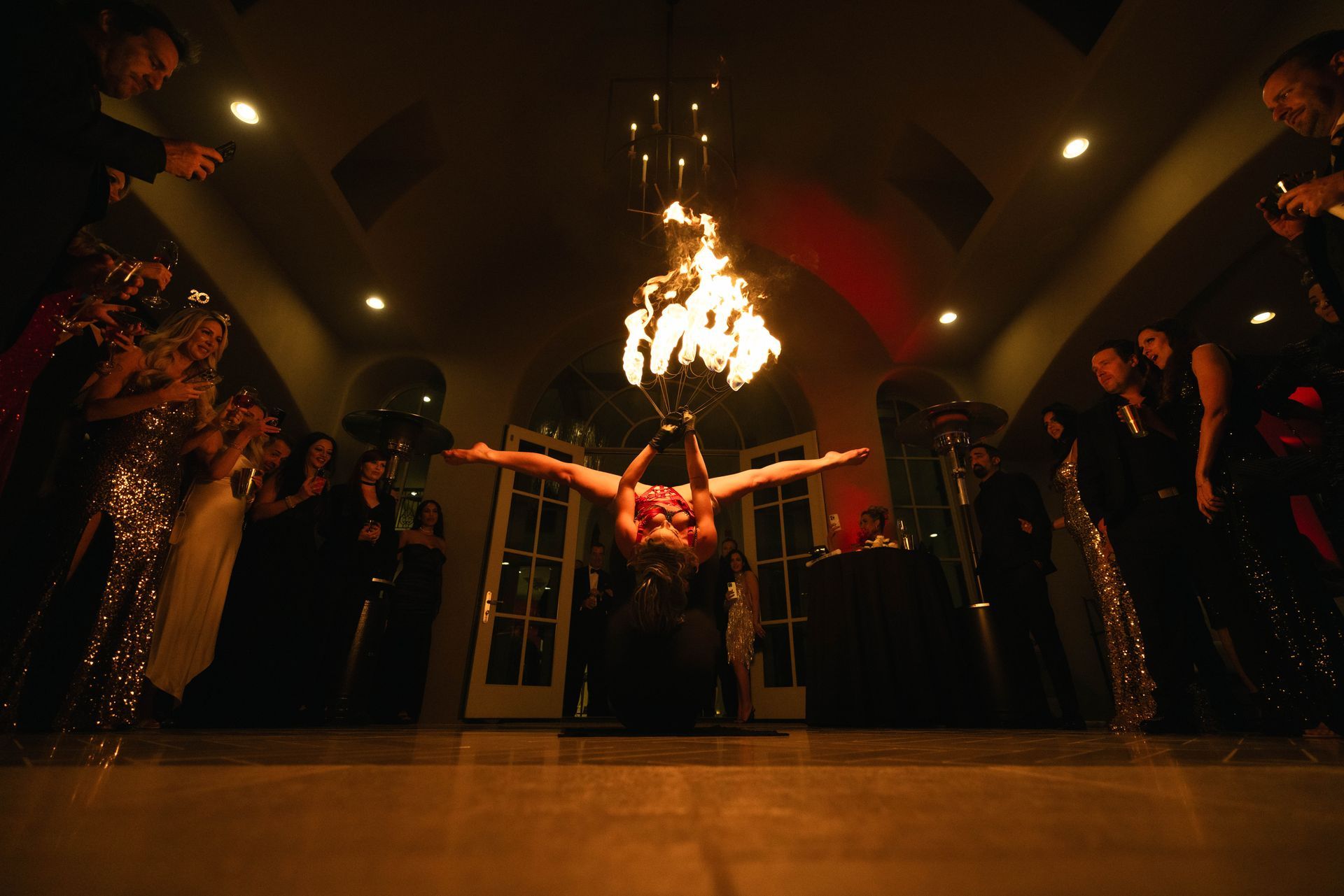 A woman is doing a handstand in front of a chandelier with fire coming out of it.
