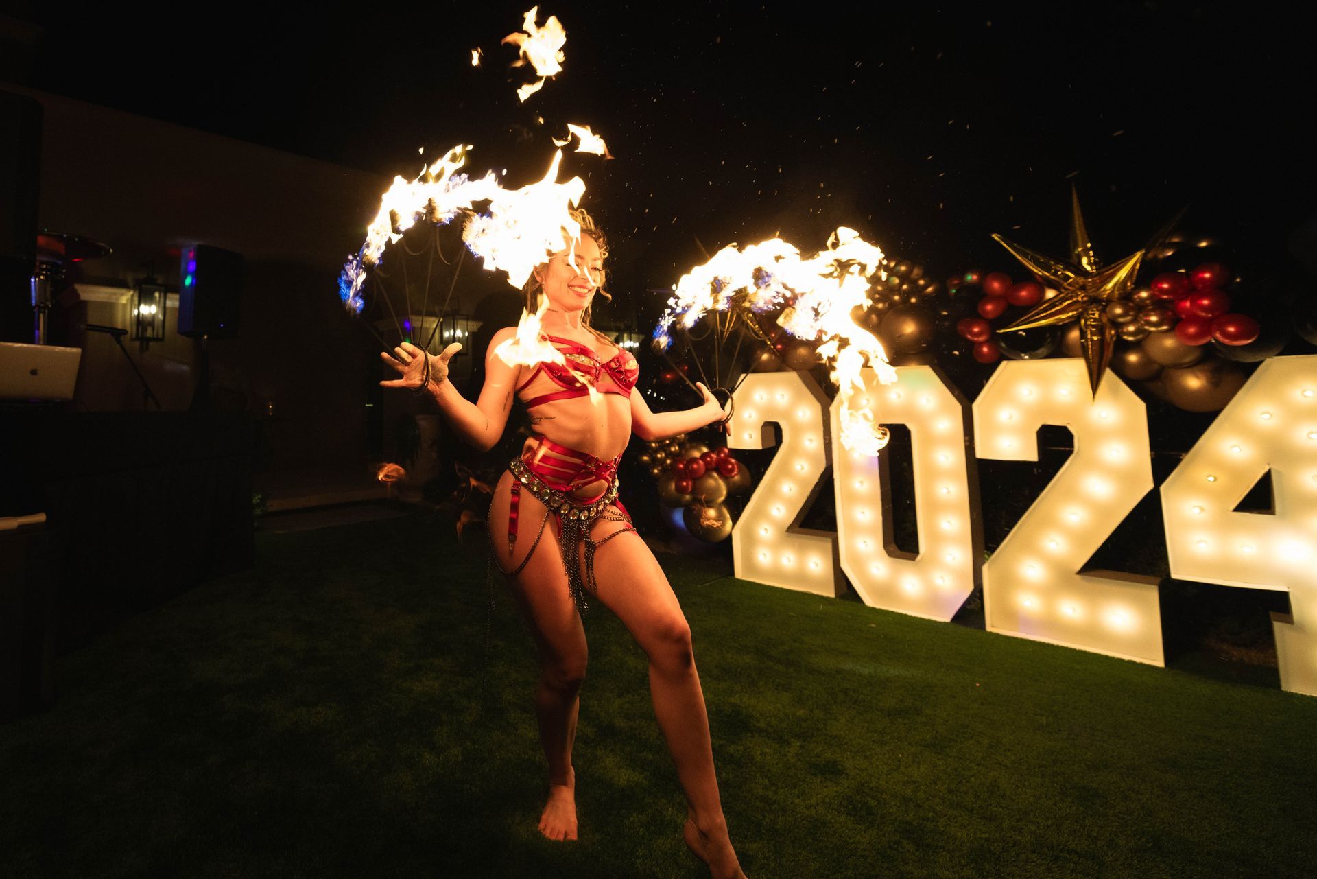 A woman is dancing with fire in front of a sign that says 2024.