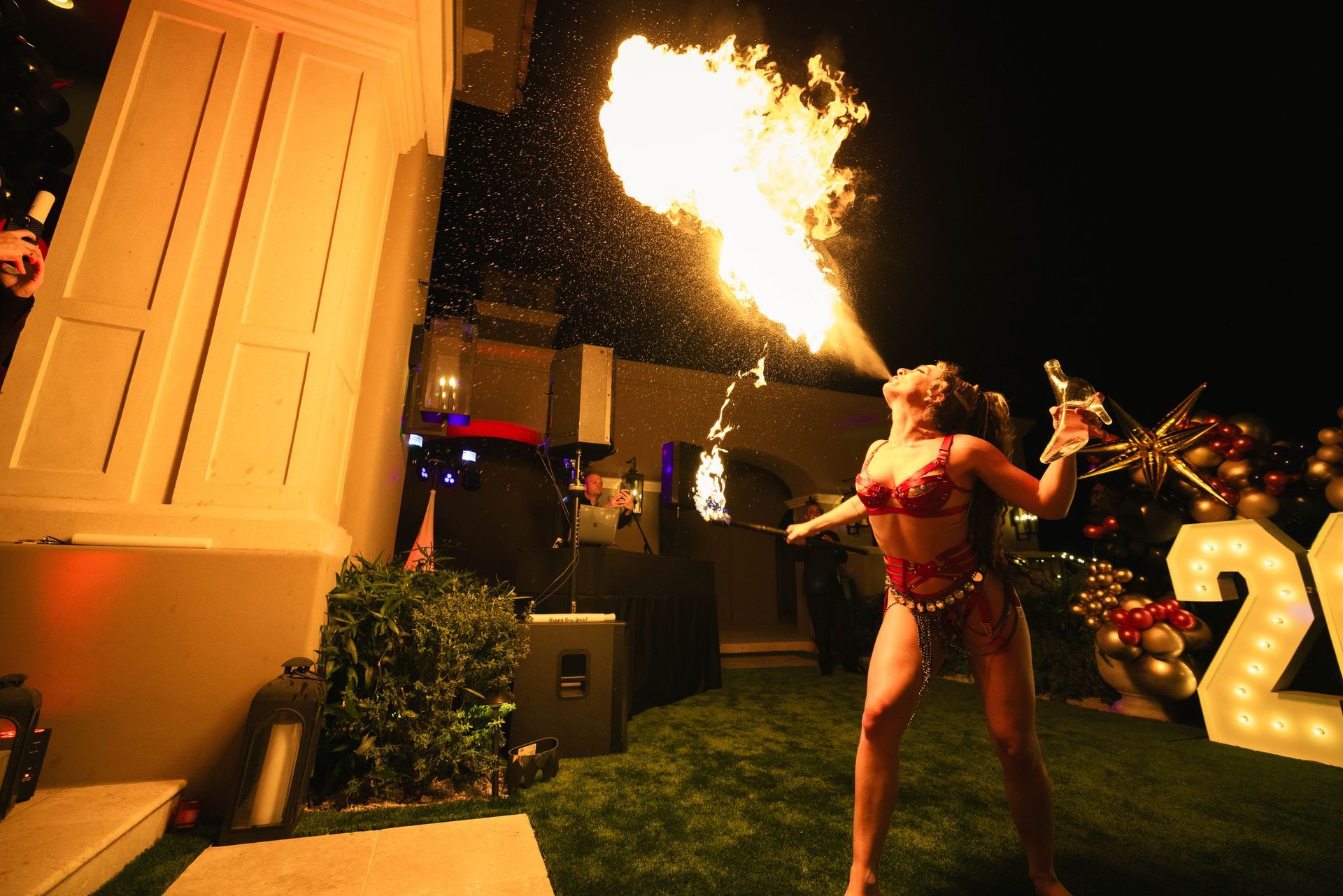 A woman is holding a bottle of champagne and blowing flames out of her mouth.