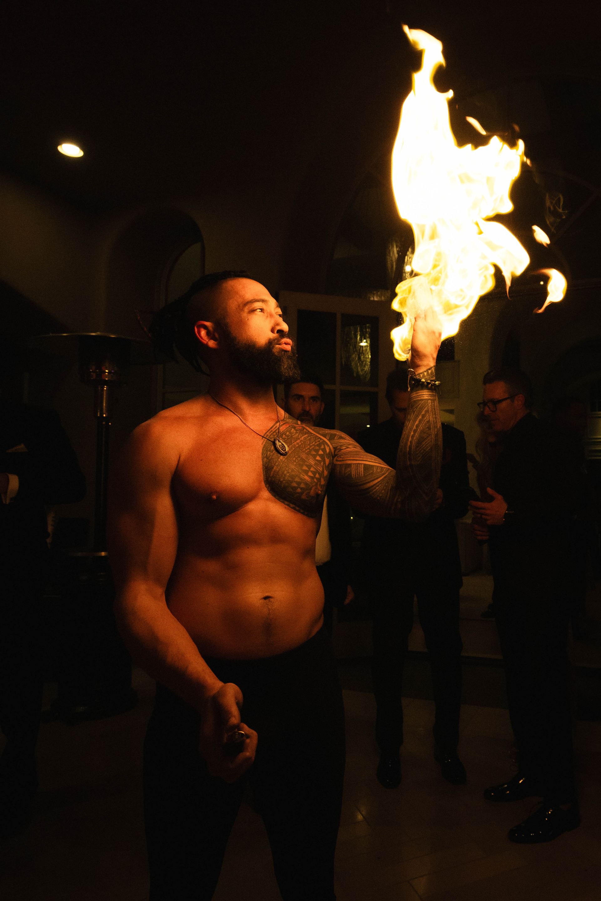 A shirtless man is holding a torch with flames coming out of it.