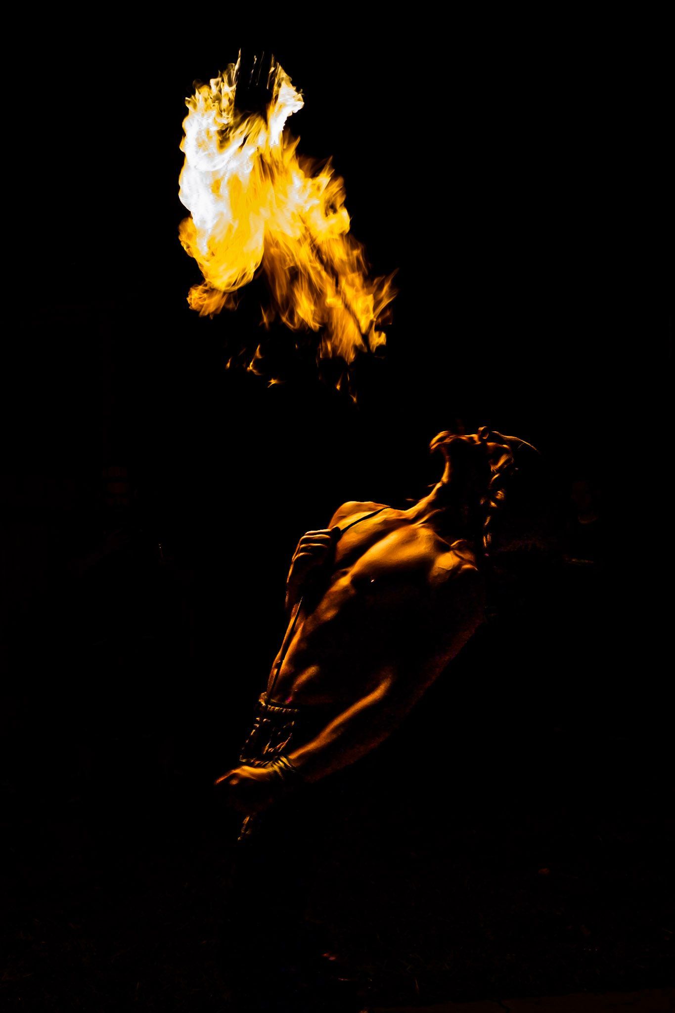 A man is blowing fire from his mouth in the dark.