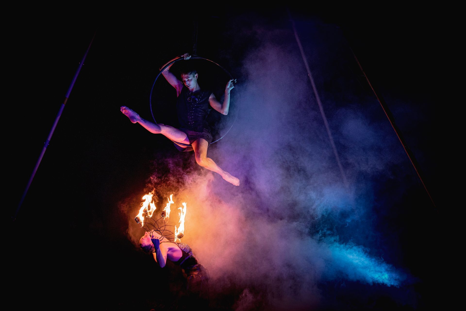 A woman is flying through the air in an aerial hoop with fire.
