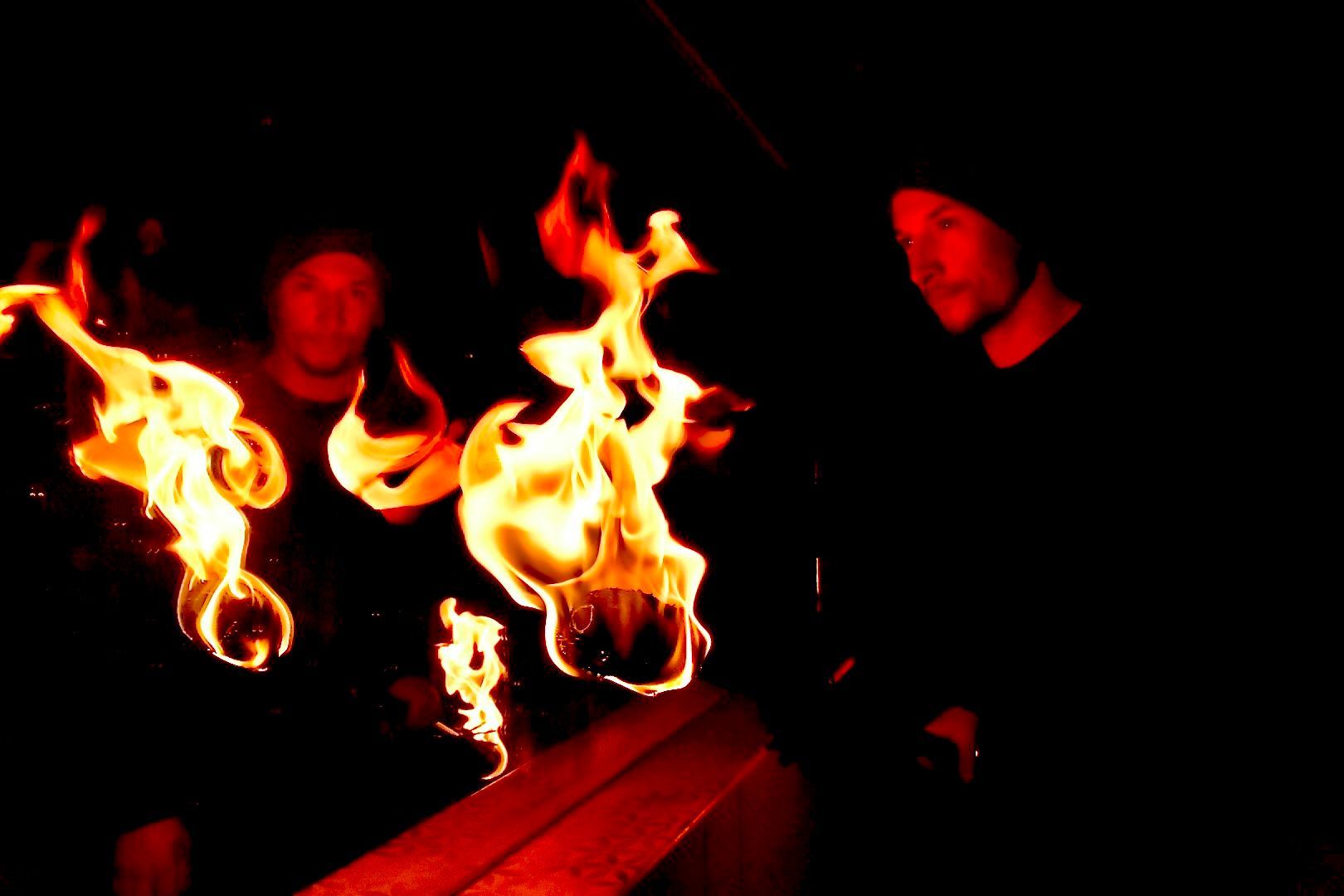 Two people are standing in front of a fire in the dark