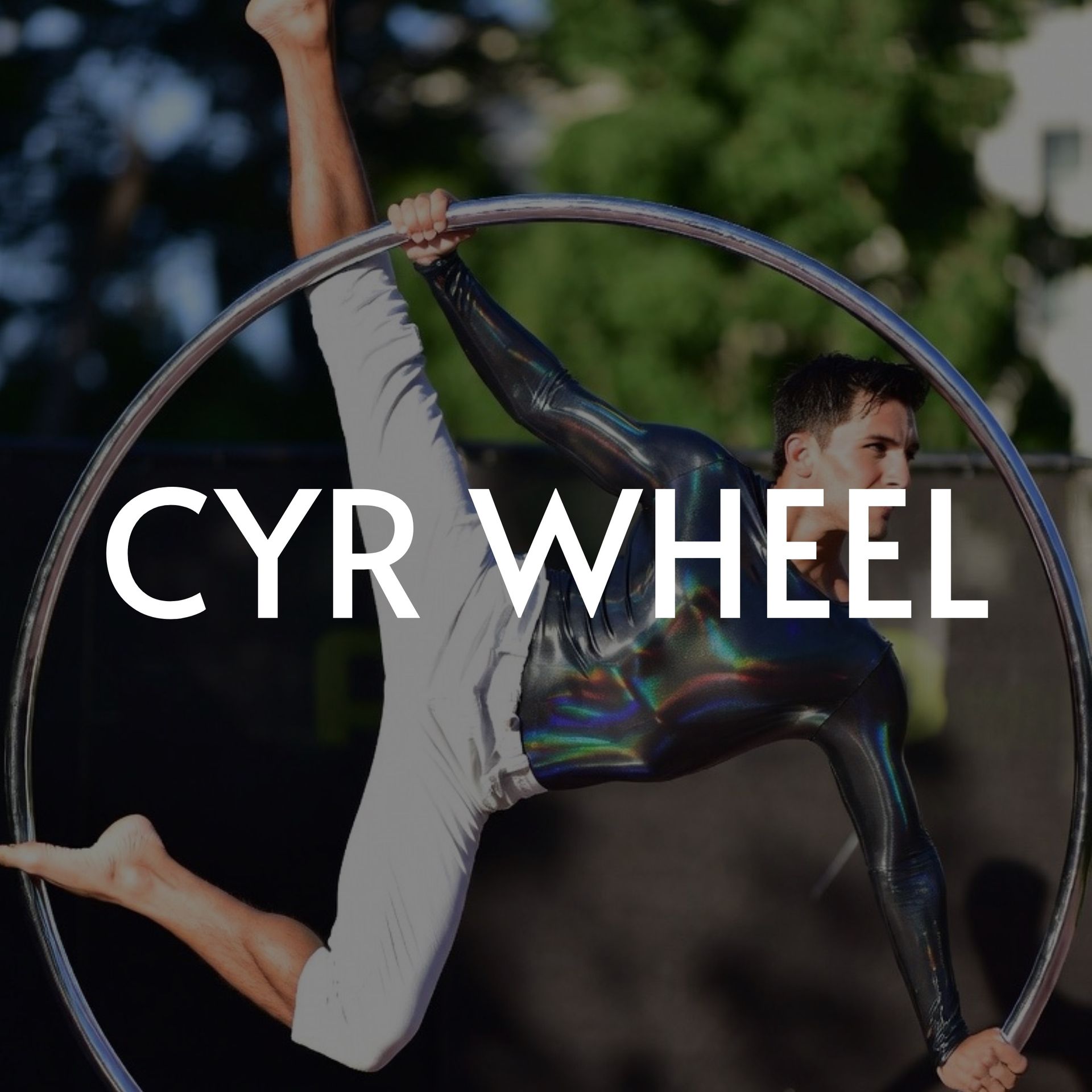 Man performing on a Cyr wheel, wearing silver bodysuit and white pants, outdoors, legs split.
