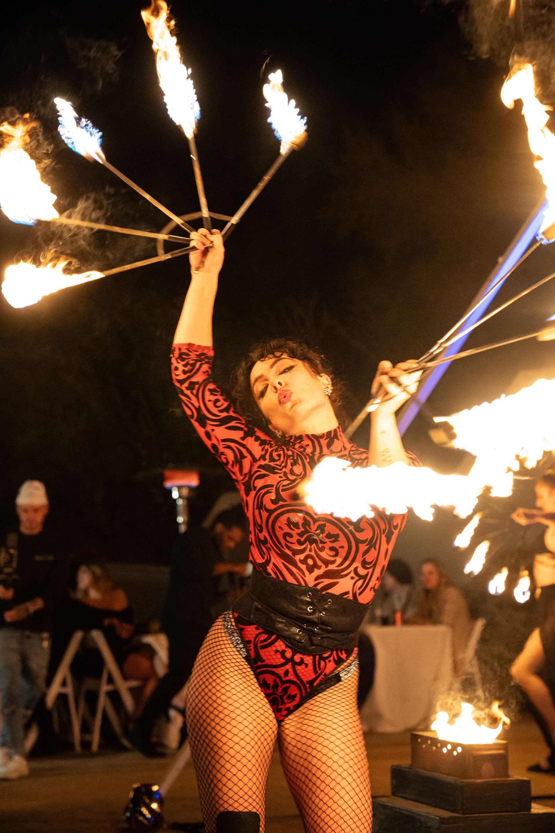 A woman in a red bodysuit is holding a fan of fire.