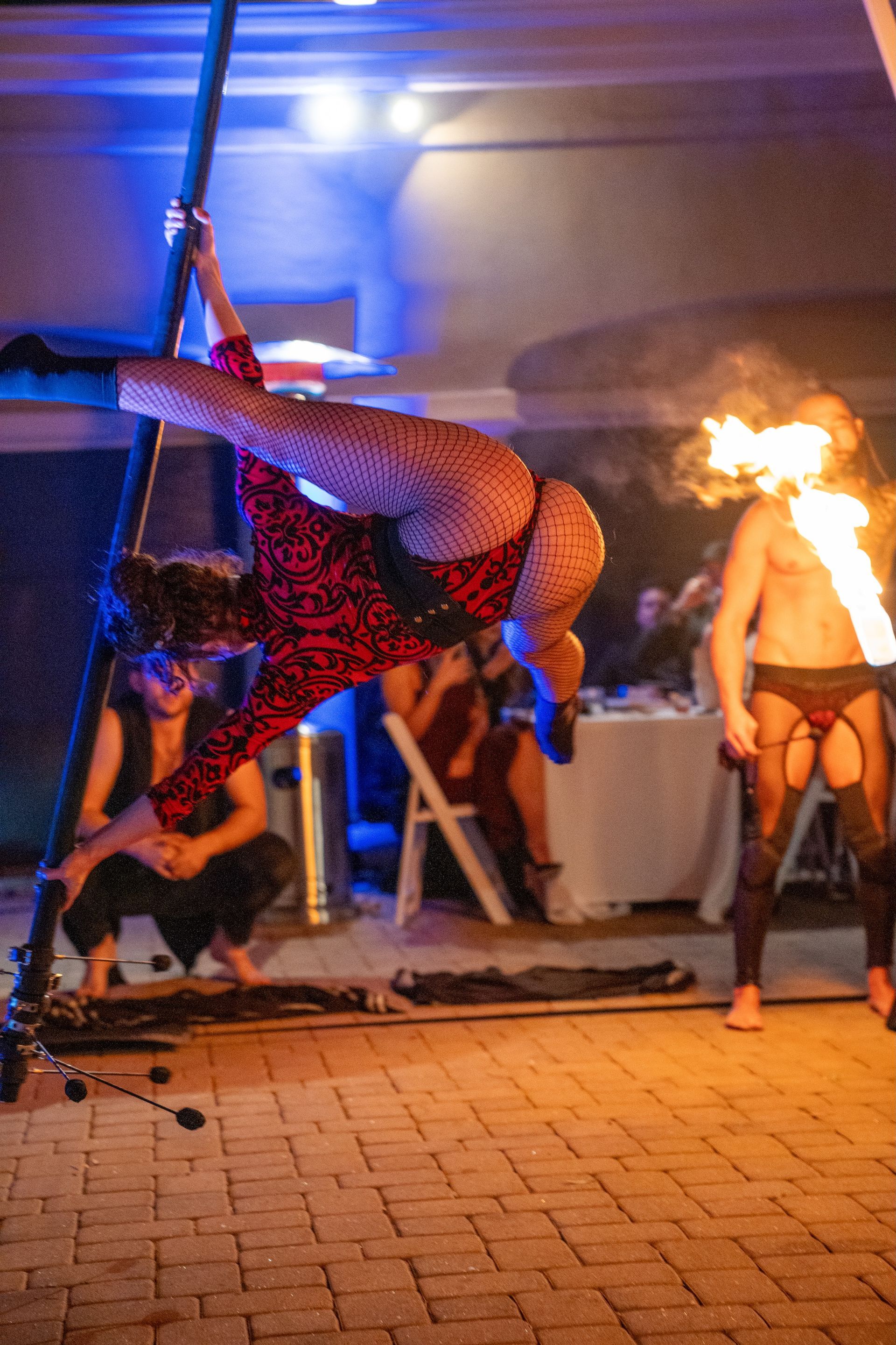 A woman is doing a split on a pole while a man holds a fire torch.