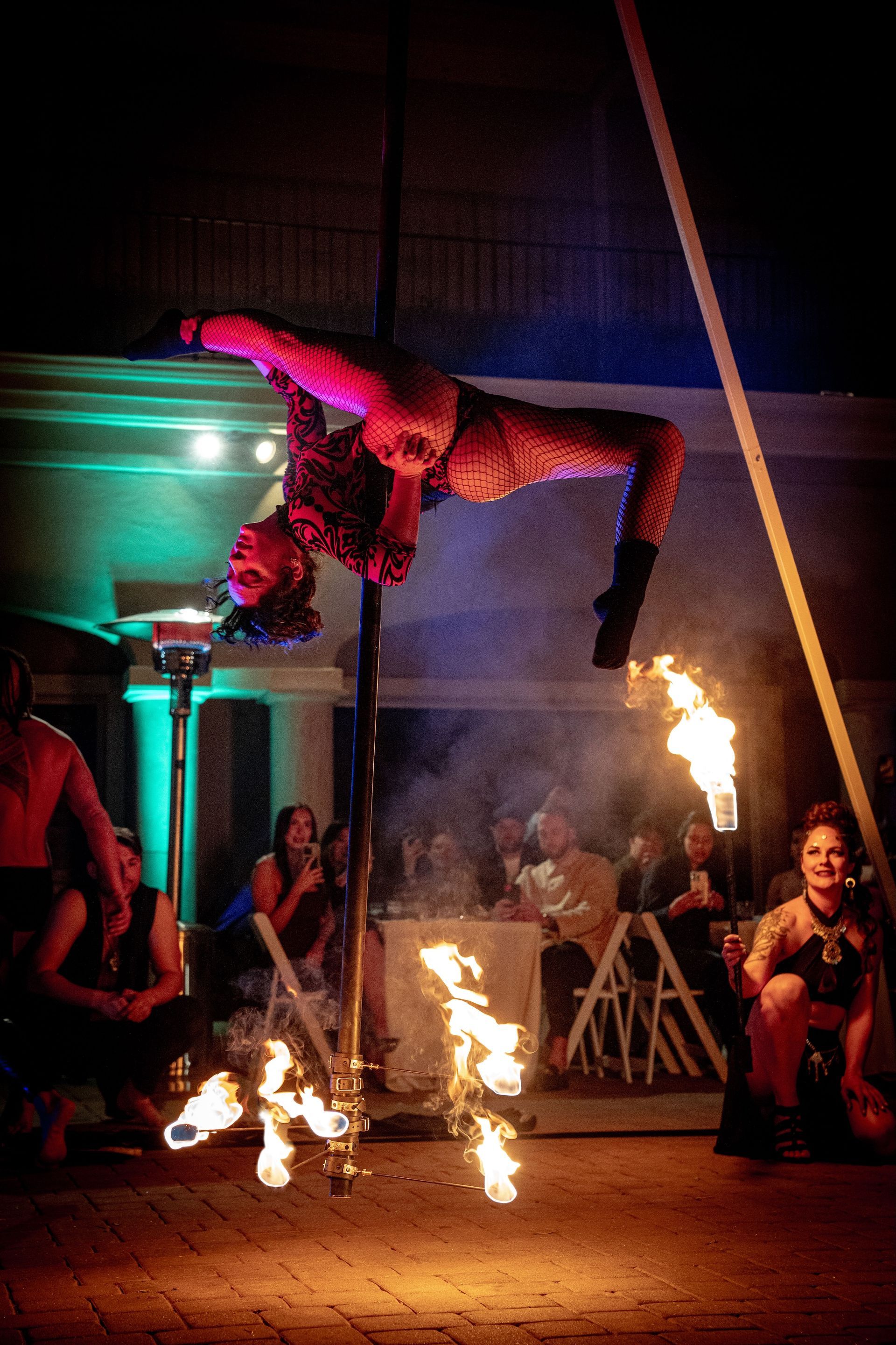 A woman is performing aerial acrobatics on a pole while people watch.
