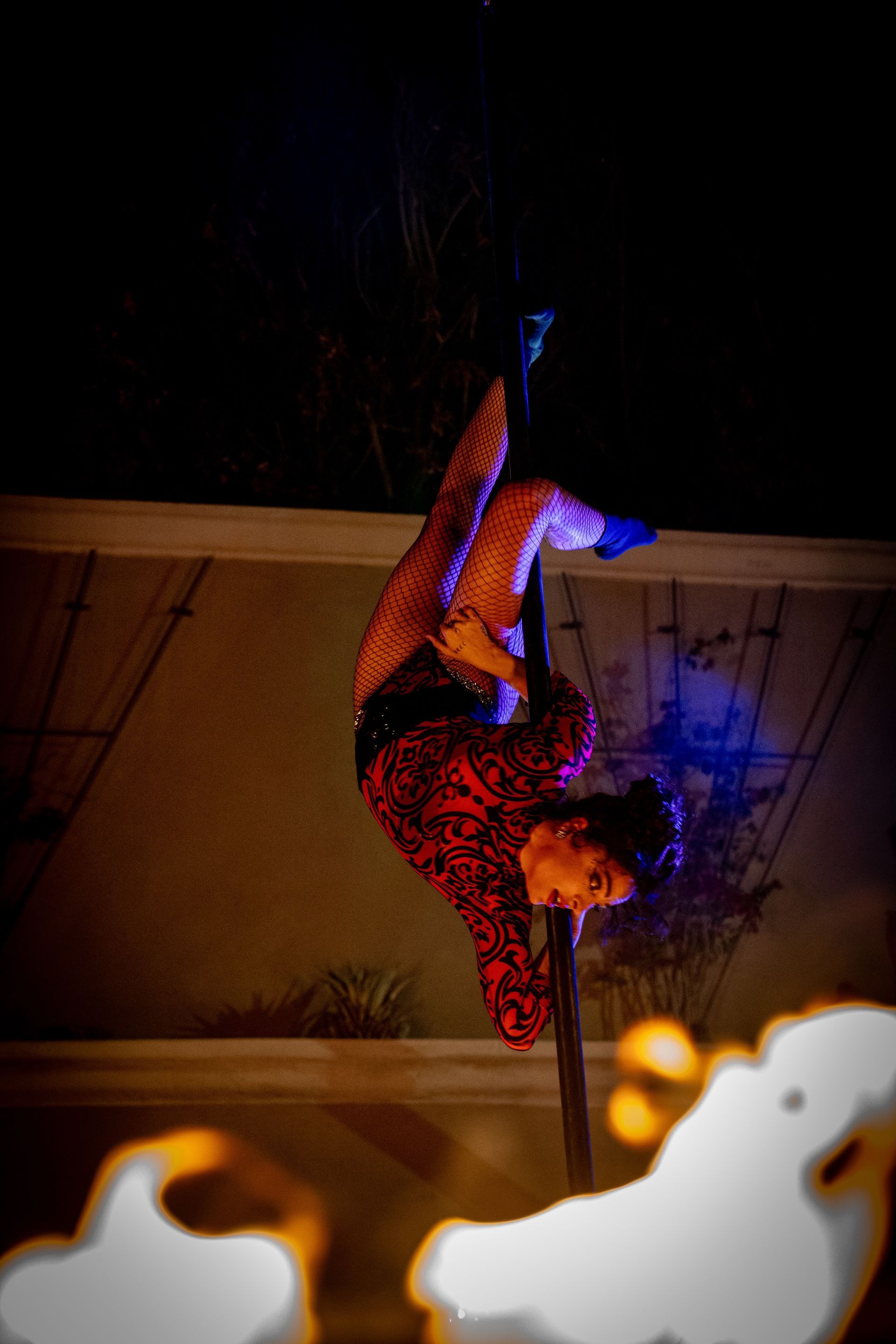 A woman is doing aerial acrobatics on a pole at night.