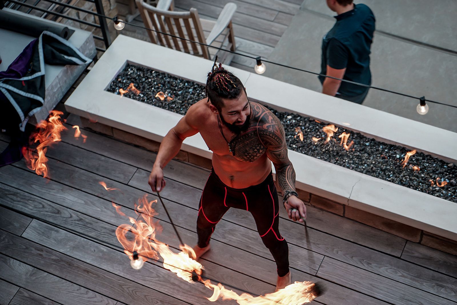 A shirtless man is holding a stick of fire on a deck.