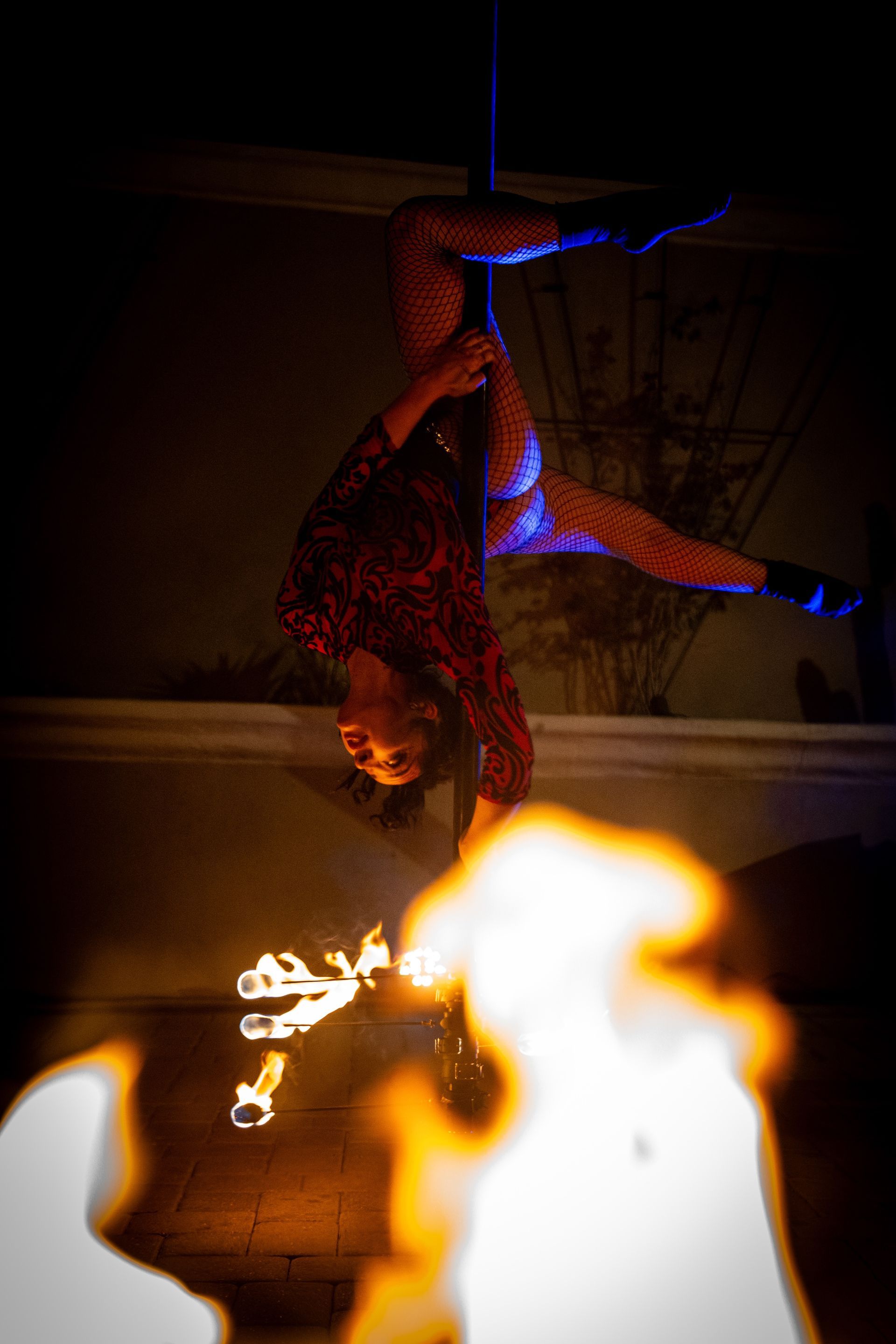 A woman is hanging upside down on a pole with fire coming out of her hands.