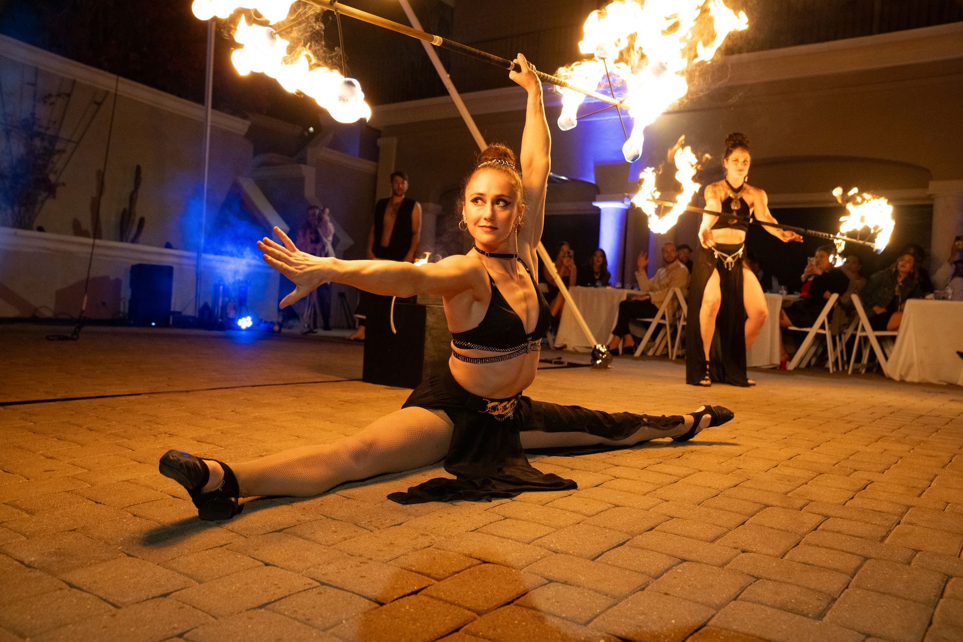 A woman is doing a split while holding a fire torch.