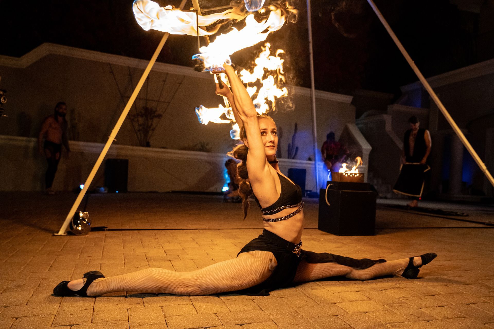 A woman is doing a split while holding a fire torch.