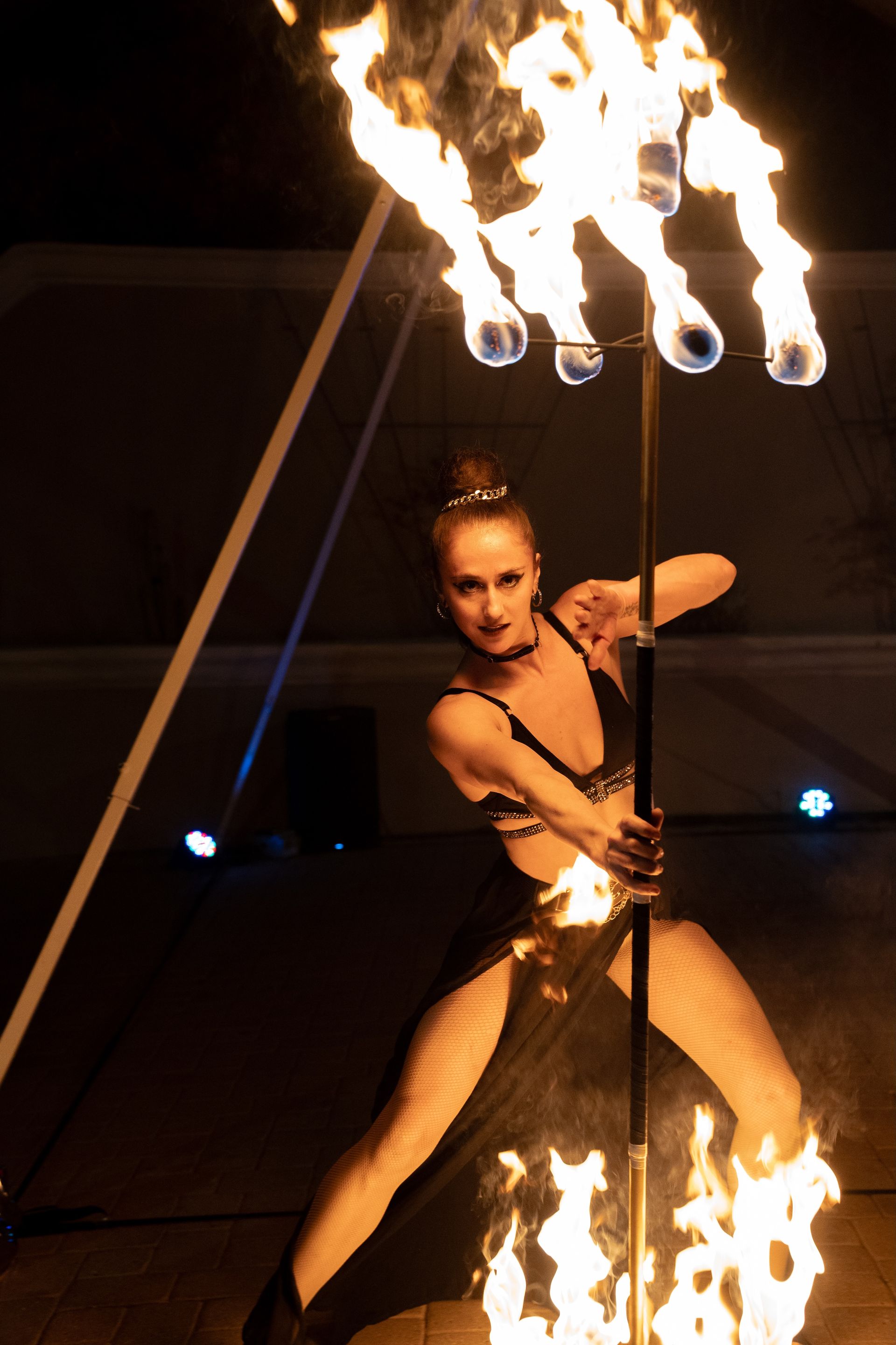 A woman in a black dress is holding a pole with flames coming out of it.