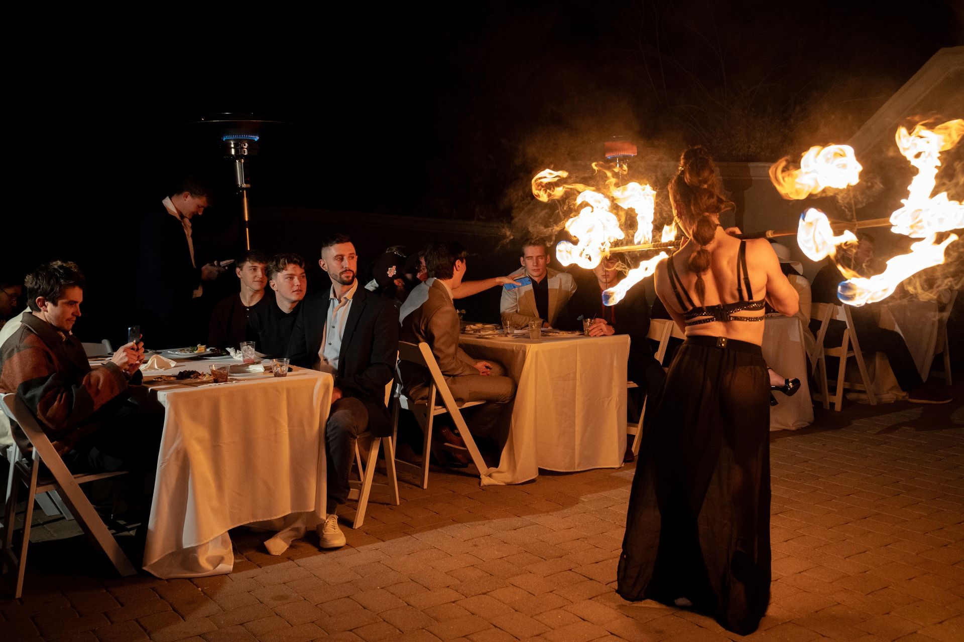 A group of people are sitting at tables watching a fire show.