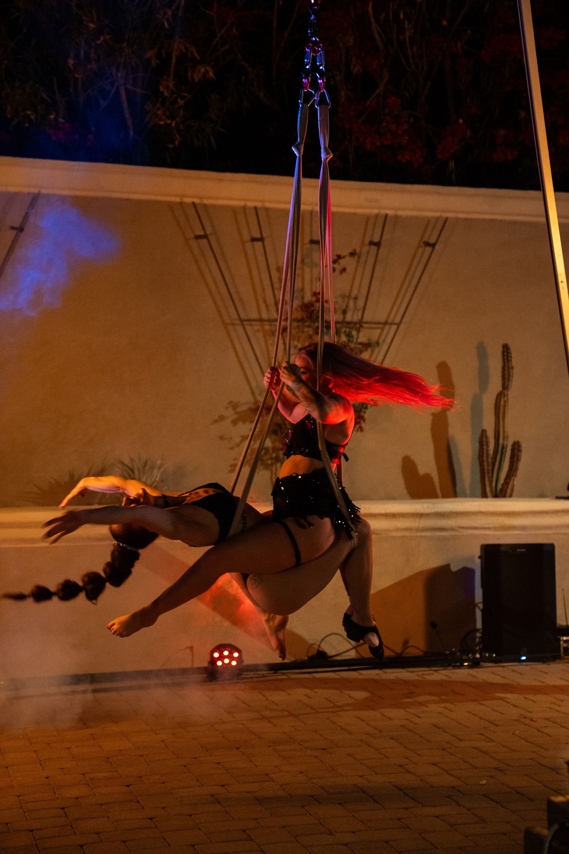 Two women are performing aerial acrobatics in a dark room.