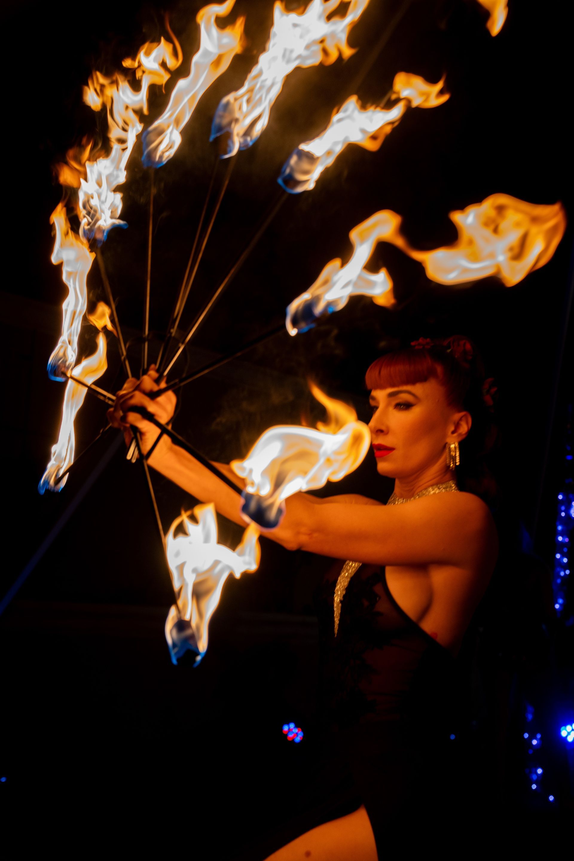 A woman is holding a fan of fire in her hands in the dark.