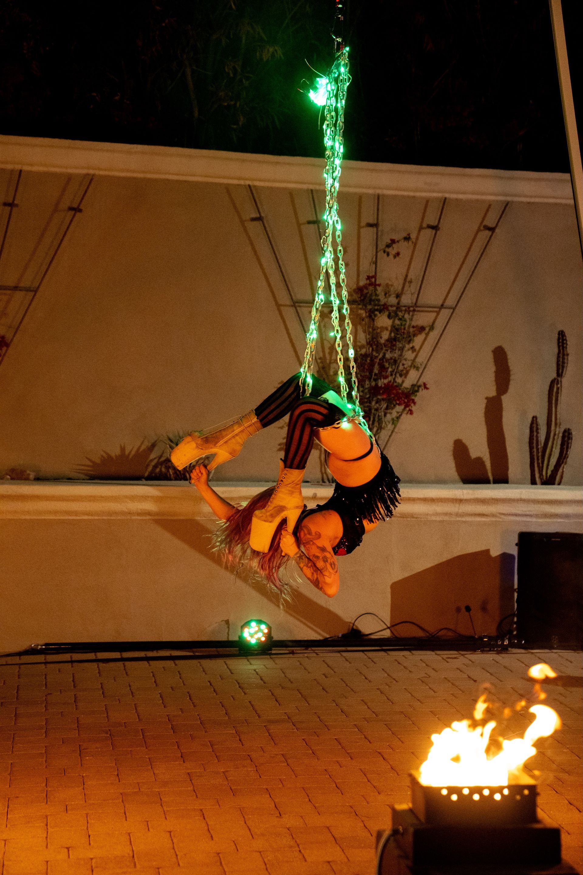 A woman is doing a handstand on a rope with green lights hanging from it.