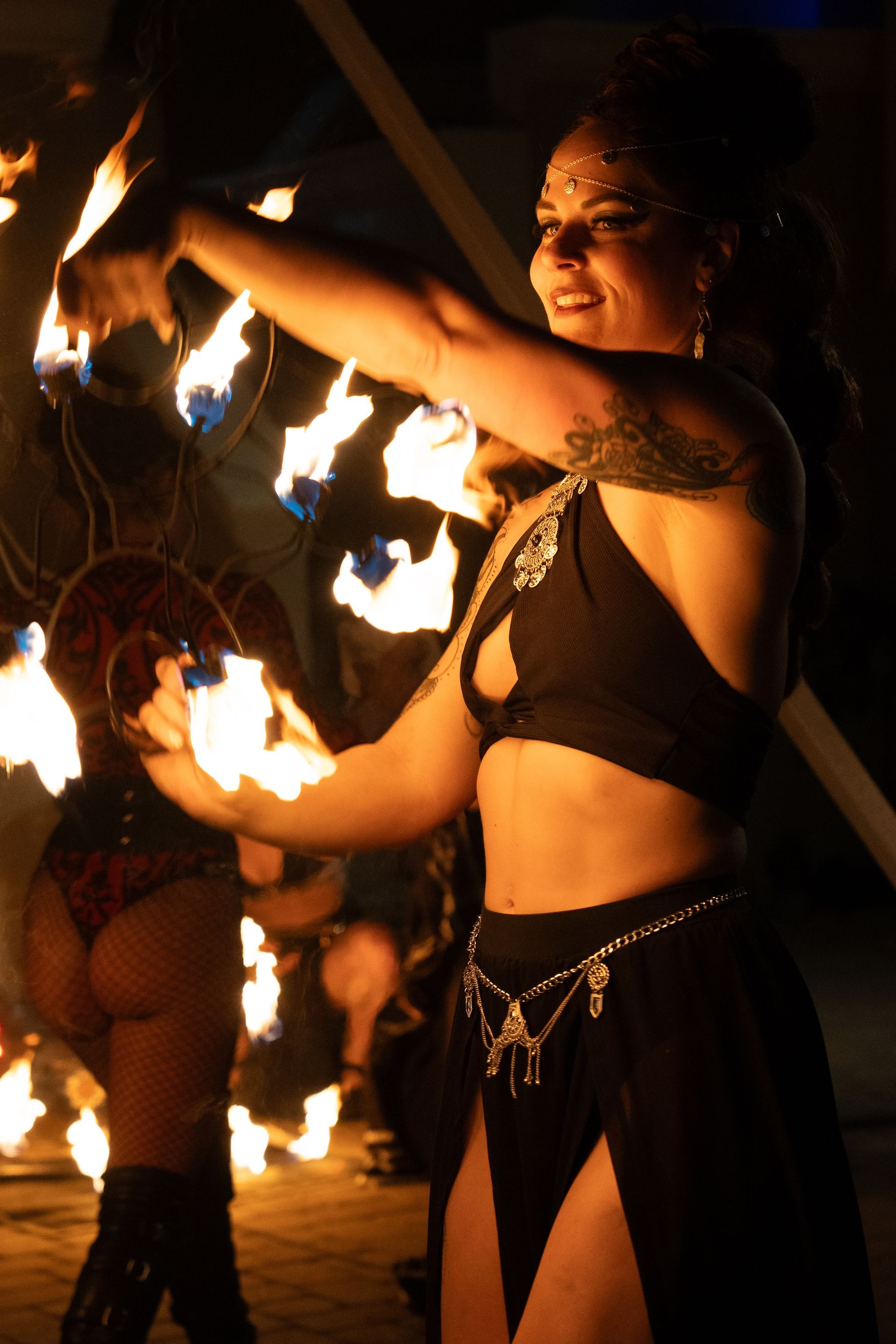 A woman in a black top and skirt is holding a torch with flames coming out of it.