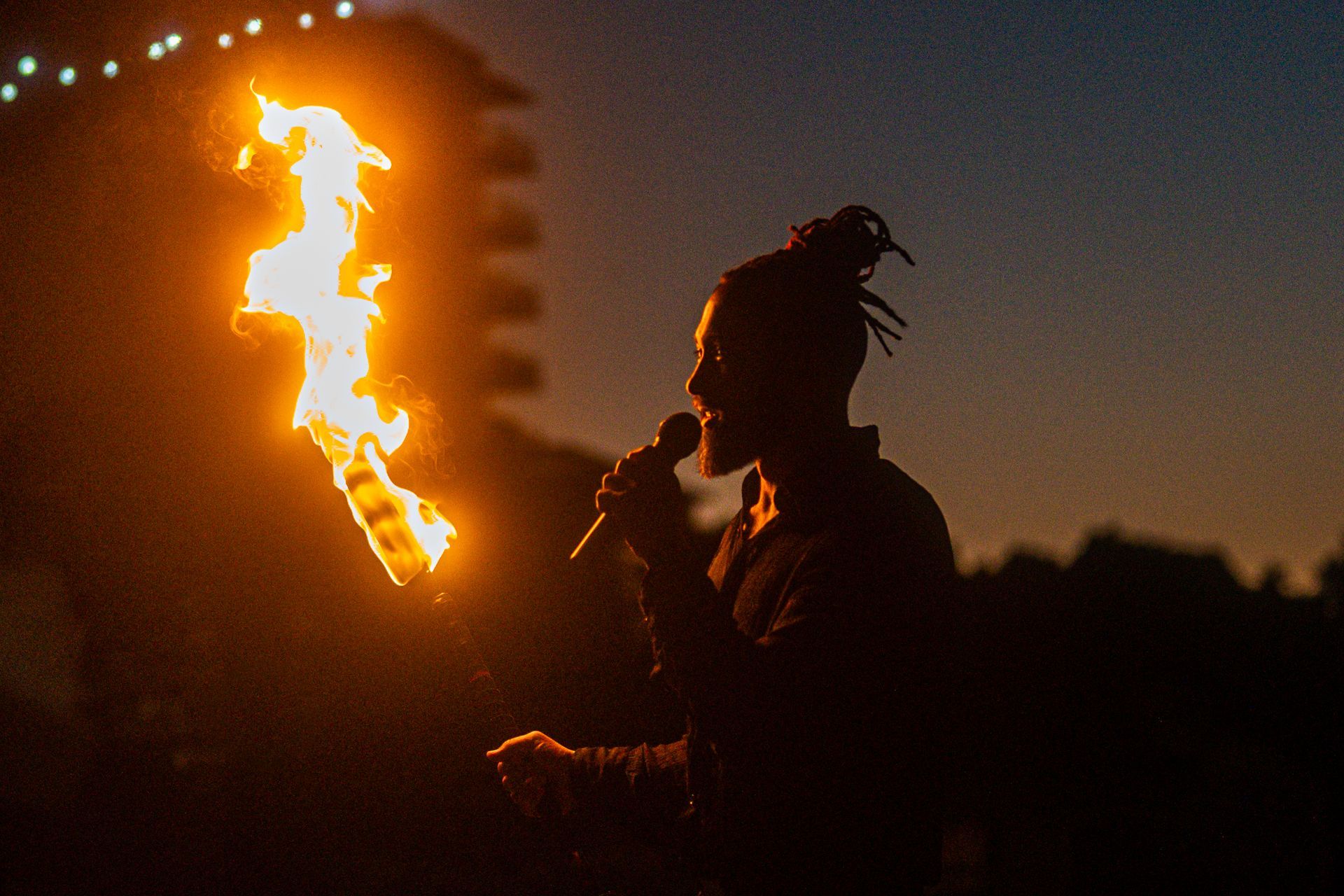 A man is holding a torch in his hand and singing into it at night.