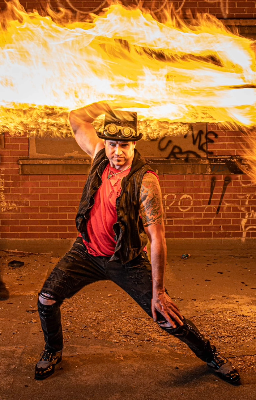 A man is holding a torch of fire in front of a brick wall.